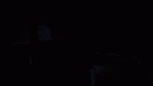 a woman in a purple shirt is sitting in a dark room with her hand on her face .