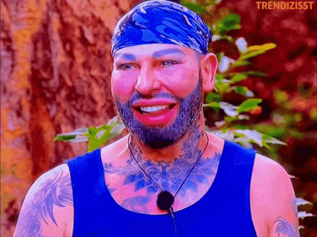 a man with a beard and tattoos wearing a blue tank top and a headband with trendizisst written on the bottom