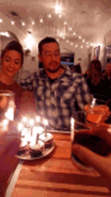 a man and woman are sitting at a table with cupcakes and candles on it .