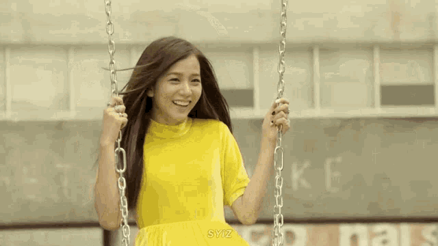a girl in a yellow dress is sitting on a swing .