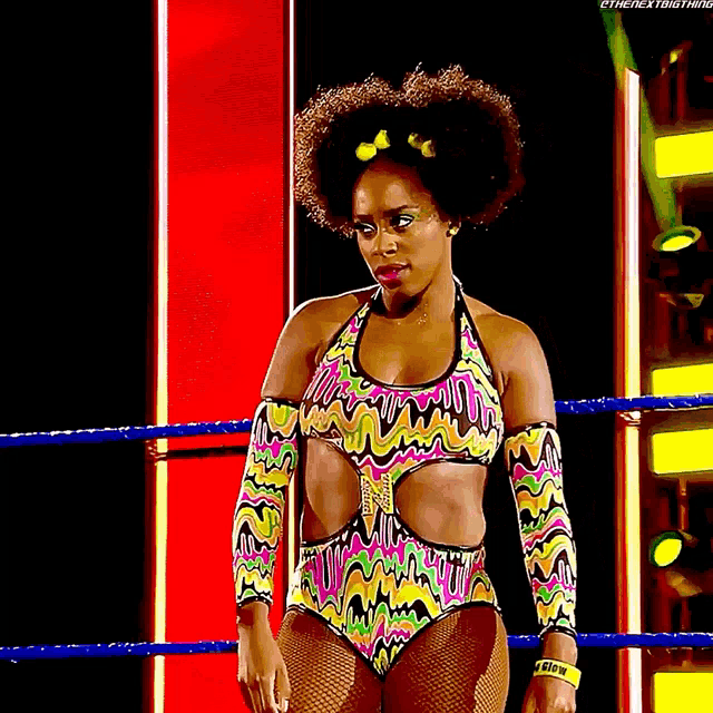 a female wrestler in a colorful outfit is standing in a wrestling ring