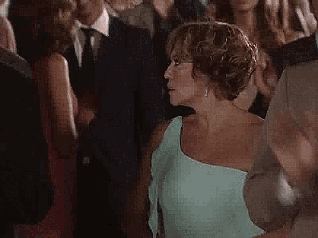 a woman in a green dress is standing in a crowd of people and making a funny face .
