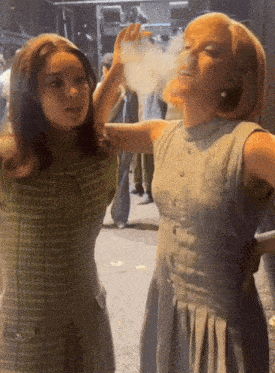 two women are standing next to each other and one is blowing smoke out of her mouth