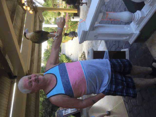 a man holding a bird on his arm while wearing a striped tank top