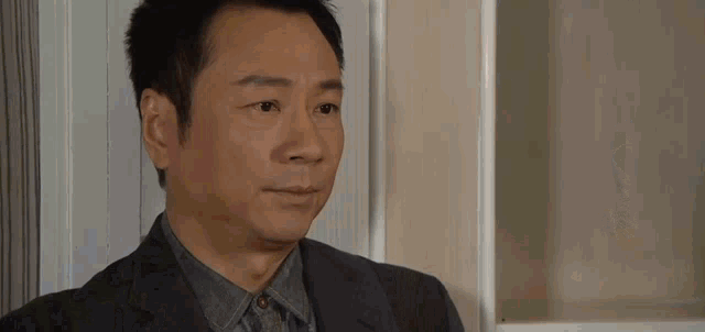 a man in a suit and tie is standing in front of a bookshelf and looking at the camera .