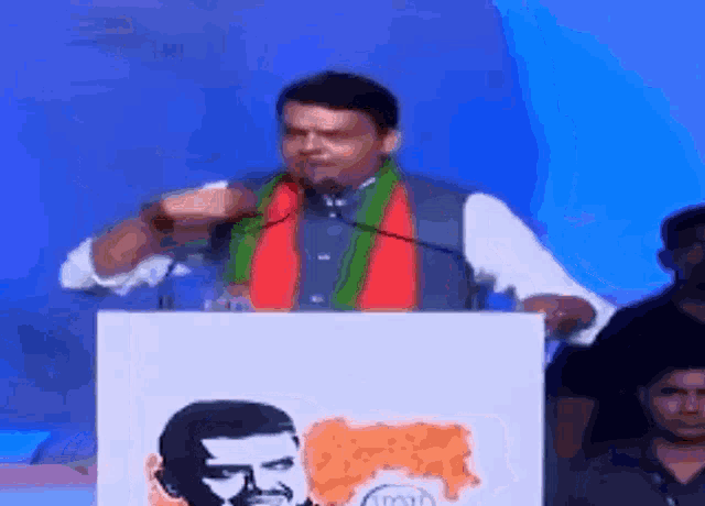 a man is giving a speech at a podium with a picture of a man in the background