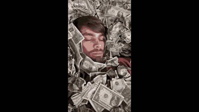 a man is laying in a pile of money and looking at the camera .