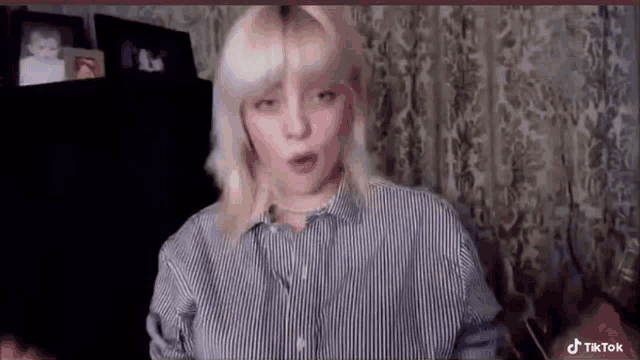 a woman with blonde hair and a striped shirt is sitting in front of a curtain .