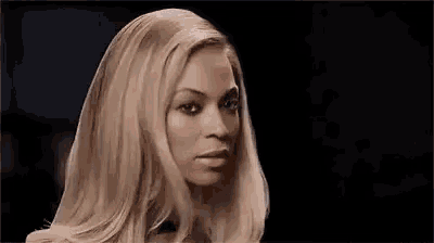 a close up of a woman 's face with long blonde hair and a black background .