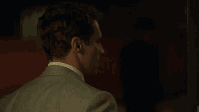 a man in a suit and tie looks at the camera with a red background