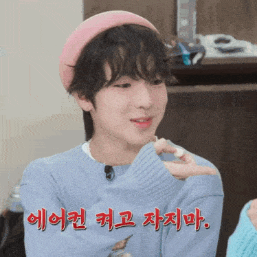 a young boy wearing a pink hat and a blue sweater has korean writing on his chest
