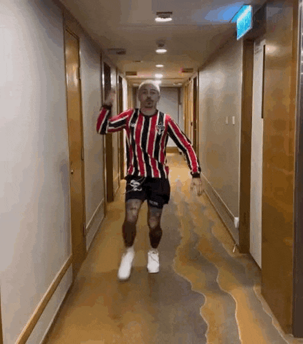 a man is dancing in a hallway wearing a striped shirt and shorts .