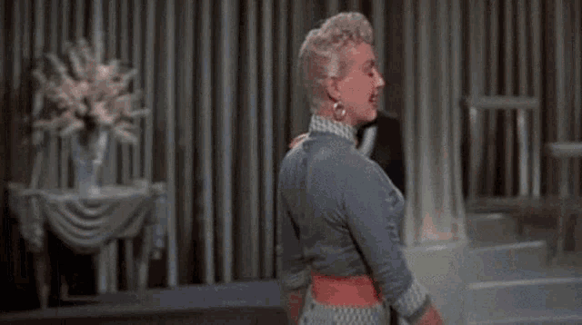 a woman in a blue dress is dancing on a stage while a woman in a black dress stands behind her .