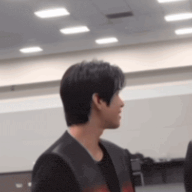 a man in a black jacket is standing in a room with ceiling lights .