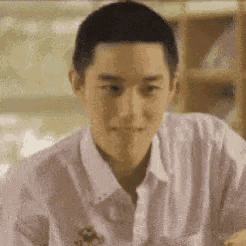 a young man in a white shirt is sitting at a table and making a face .