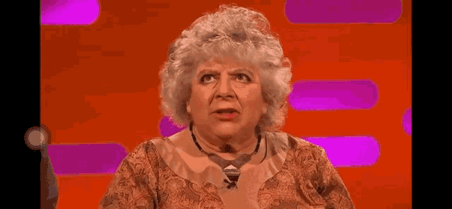 a woman with gray hair and a necklace is making a funny face on a pink and orange background .
