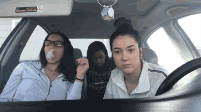 three girls in a car with a sticker on the rear view mirror that says no smoking