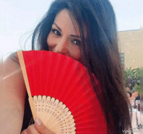 a woman is holding a red fan over her face and smiling