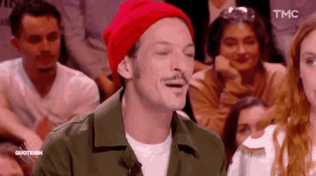 a man wearing a red hat and a green jacket is sitting in front of a crowd .
