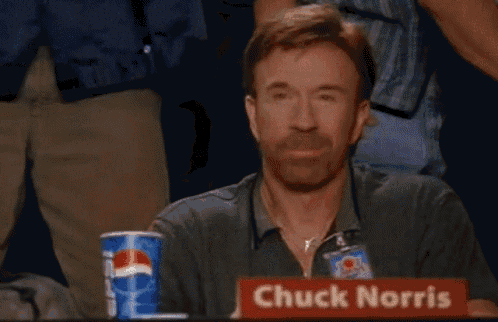 chuck norris is giving a thumbs up while sitting at a table