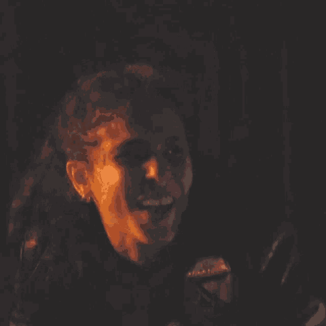 a woman is smiling in a dark room while wearing a leather jacket .