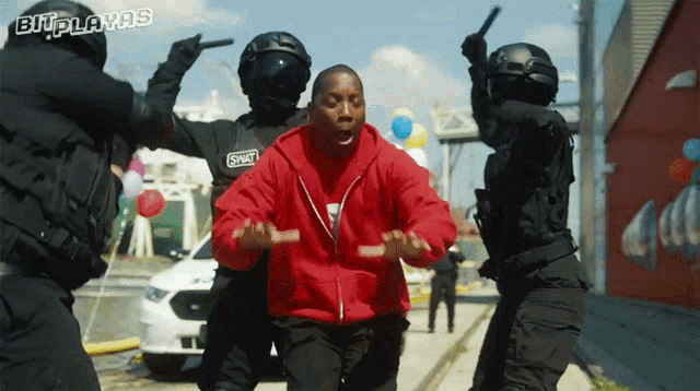 a man in a red hoodie is surrounded by swat officers holding a gun
