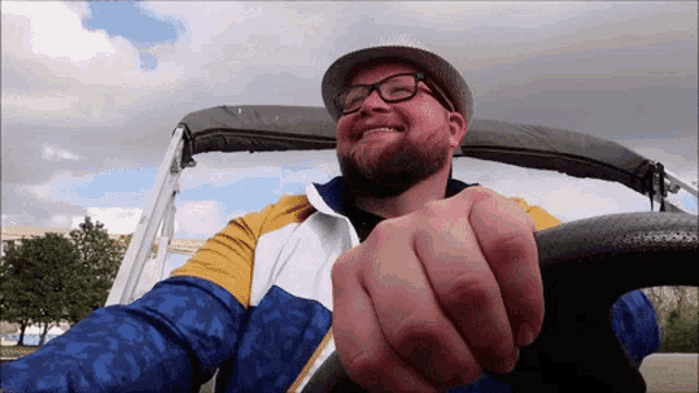 a man wearing glasses and a hat is holding a steering wheel