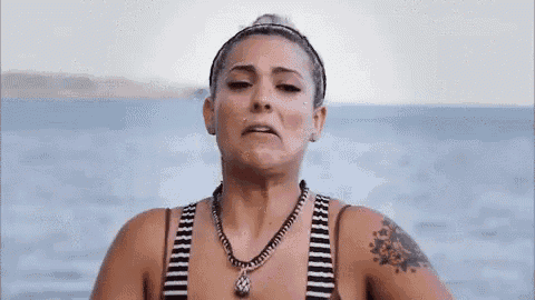 a woman in a striped bikini is standing in front of the ocean and making a funny face .