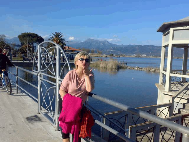 a woman blows a kiss while standing next to a railing overlooking a body of water
