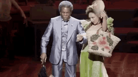 a man in a suit and a woman in a green dress are on stage holding hands