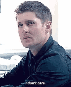 a man in a black shirt is sitting at a desk and says `` i don 't care '' .
