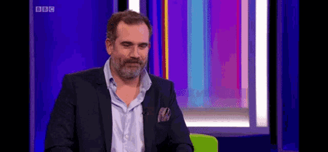 a man with a beard is sitting in front of a bbc sign
