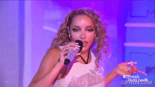 a woman is singing into a microphone while wearing a shirt that says ' nasty ' on it
