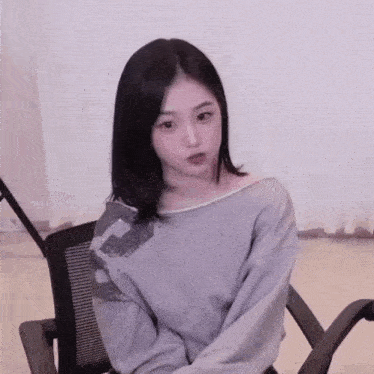 a young woman is sitting in a chair wearing a gray sweater and making a funny face .