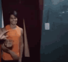 a man in an orange tank top is standing in front of a door .