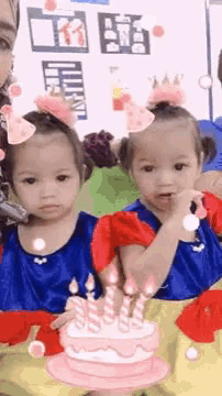 two little girls are sitting next to each other in front of a birthday cake .