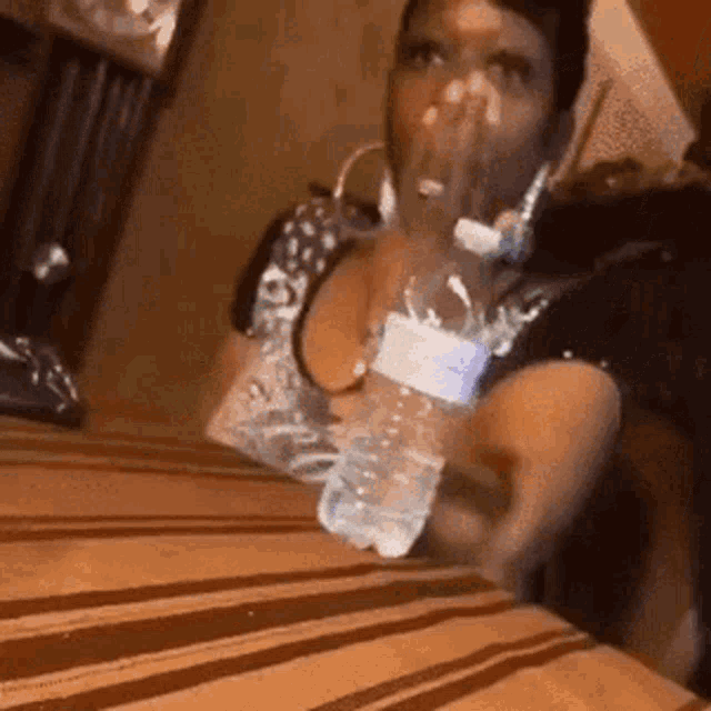a woman is sitting at a table with a bottle of water covering her mouth .