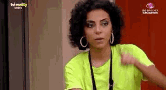 a woman with curly hair is wearing a neon yellow t-shirt and earrings .