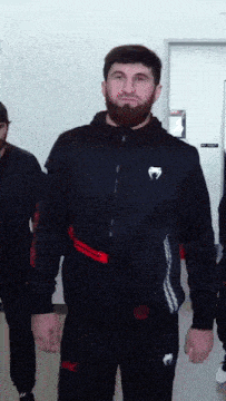 a man with a beard is wearing a black jacket with a white logo that says venum
