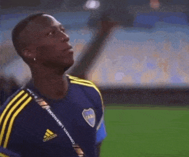a man in a blue and yellow adidas shirt is standing on a field .