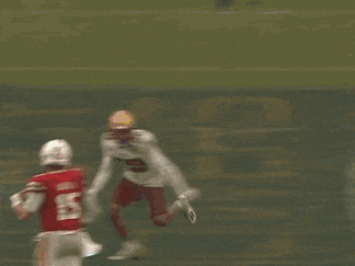 a football player in a red jersey and white pants is being tackled by another player on the field .