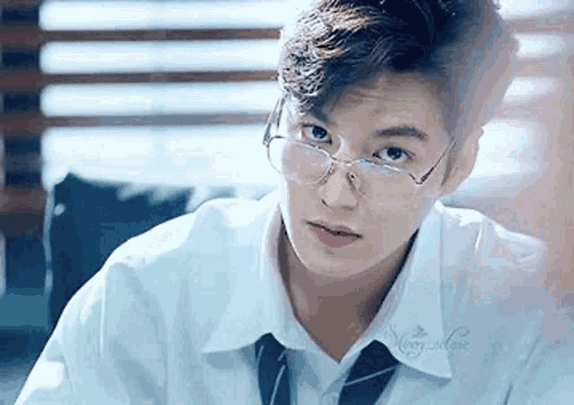 a young man wearing glasses and a tie is sitting at a desk .