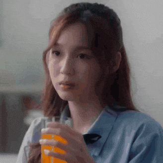 a young woman is drinking a glass of orange juice .