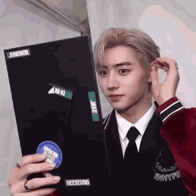 a young man in a suit and tie is holding a sticker with the name heeseung on it
