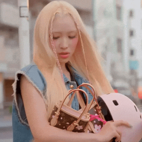 a woman with blonde hair is holding a purse and a helmet