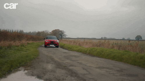 a red car is driving down a dirt road with car written on the bottom right