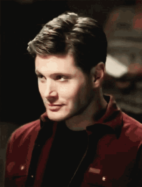 a close up of a man wearing a red jacket and black shirt