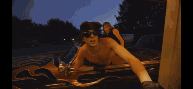 a shirtless man in a car with flames on the side