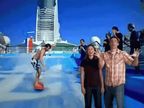 a man and a woman are standing in front of a wave pool while a man rides a surfboard