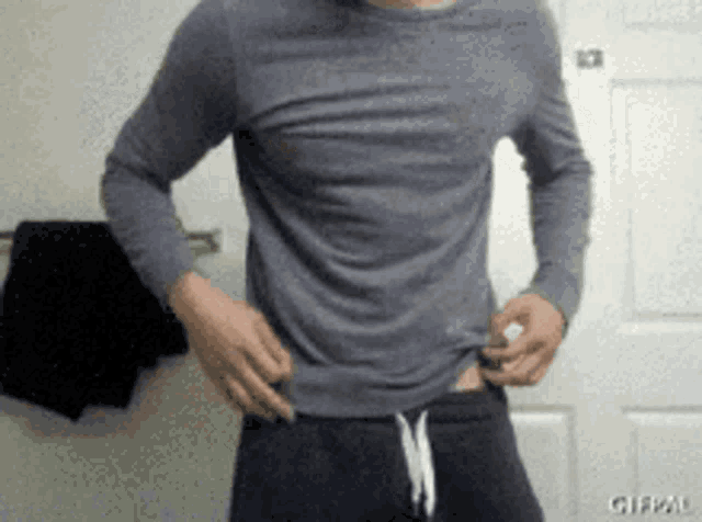 a man in a grey shirt and black shorts is standing in front of a door .